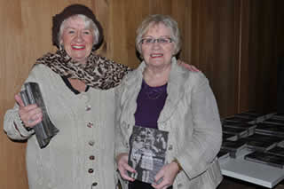 Marie Redmond & Irene Redmond who appeared as children on the cover of the book stand by a stack of the books. 